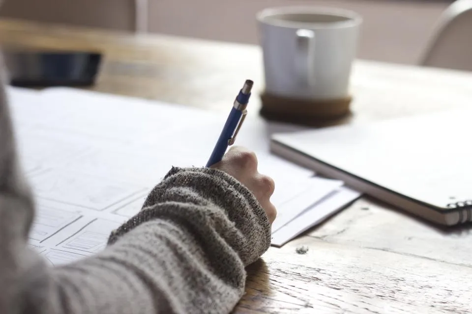 Un élève prend des notes à son bureau, une tasse posée à côté